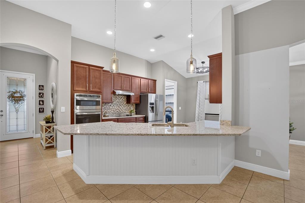 A kitchen features a granite-topped island, dark wood cabinets, stainless steel appliances, and tile flooring — 12153 CREEK PRESERVE DRIVE, RIVERVIEW, FL