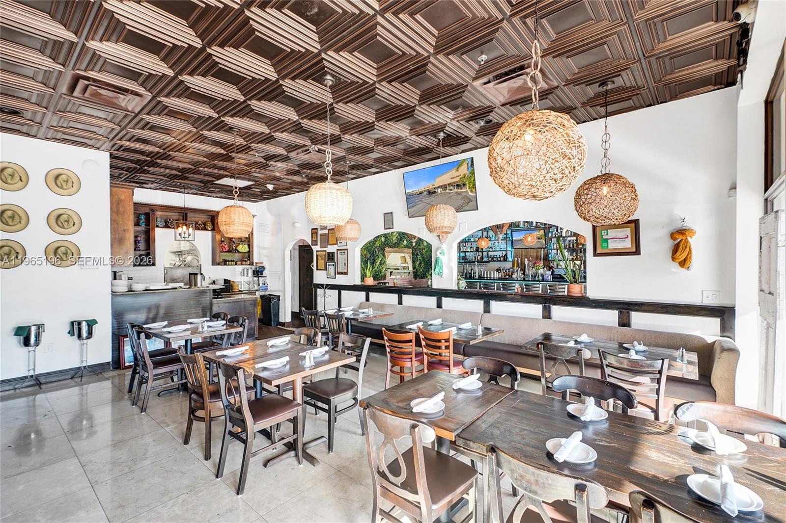 A restaurant interior features wooden tables, woven pendant lights, and a decorative coffered ceiling — 15400 Biscayne Blvd, North Miami FL 33160, NORTH MIAMI, FL