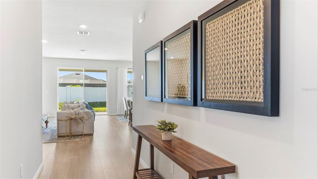 A hallway features a wooden console table, wall art, and a view into a living area — 17321 SALTBUSH TRAIL, PARRISH, FL