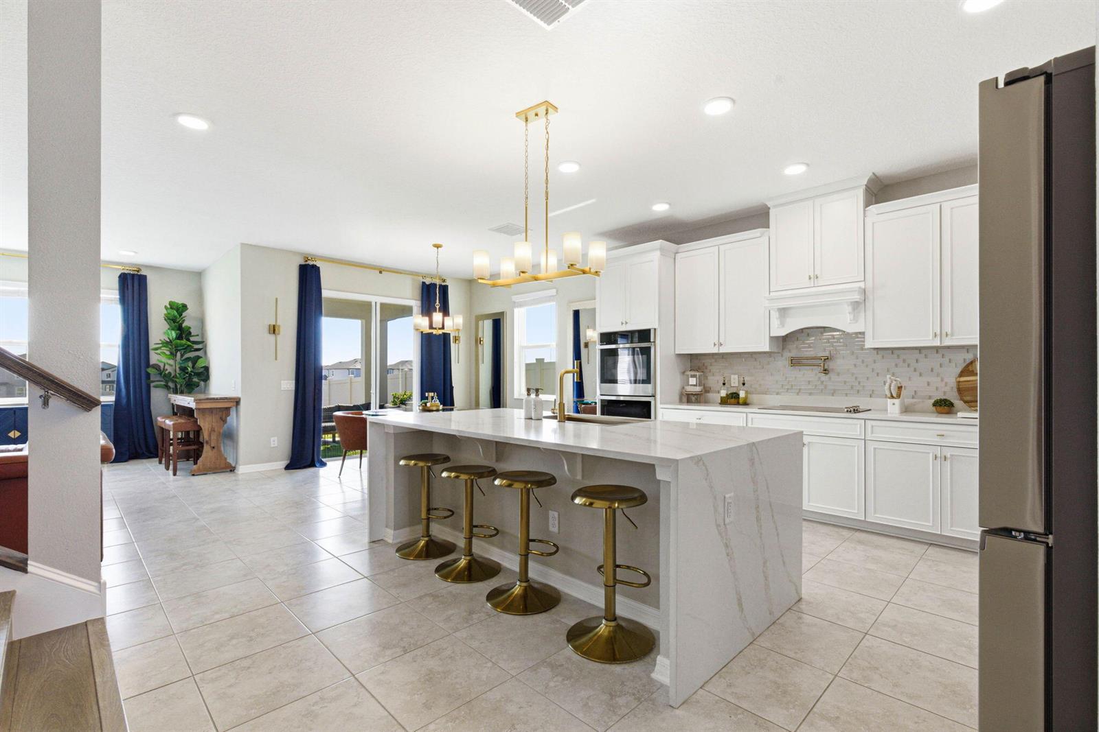 A modern kitchen features white cabinetry, a large marble-topped island, and gold bar stools — 9522 Seagrass Port Pass, FL 33545, FL