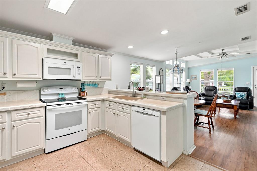 A kitchen with white cabinets, white appliances, and tile flooring opens into a living area — 5072 BUCCANEER BOULEVARD, SPRING HILL, FL