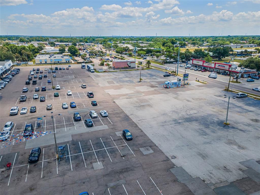 An aerial view shows a large, mostly empty asphalt parking lot with scattered cars — 7430 PALM RIVER ROAD, TAMPA, FL