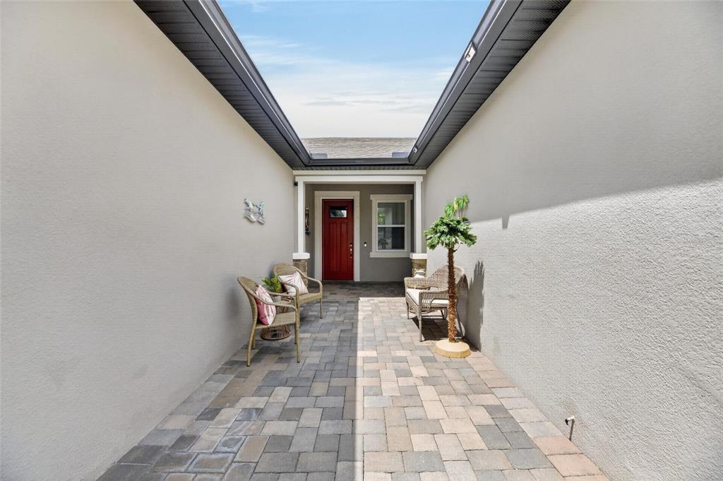 A paved courtyard leads to a red front door between two beige exterior walls — 3766 LAUGHING DOVE AVENUE, SUN CITY CENTER, FL