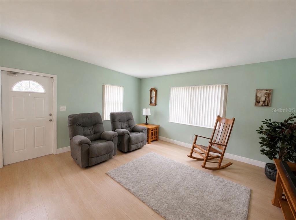 A living room features light green walls, light wood flooring, two gray recliners, and a rocker — 7812 N GOMEZ AVENUE, TAMPA, FL