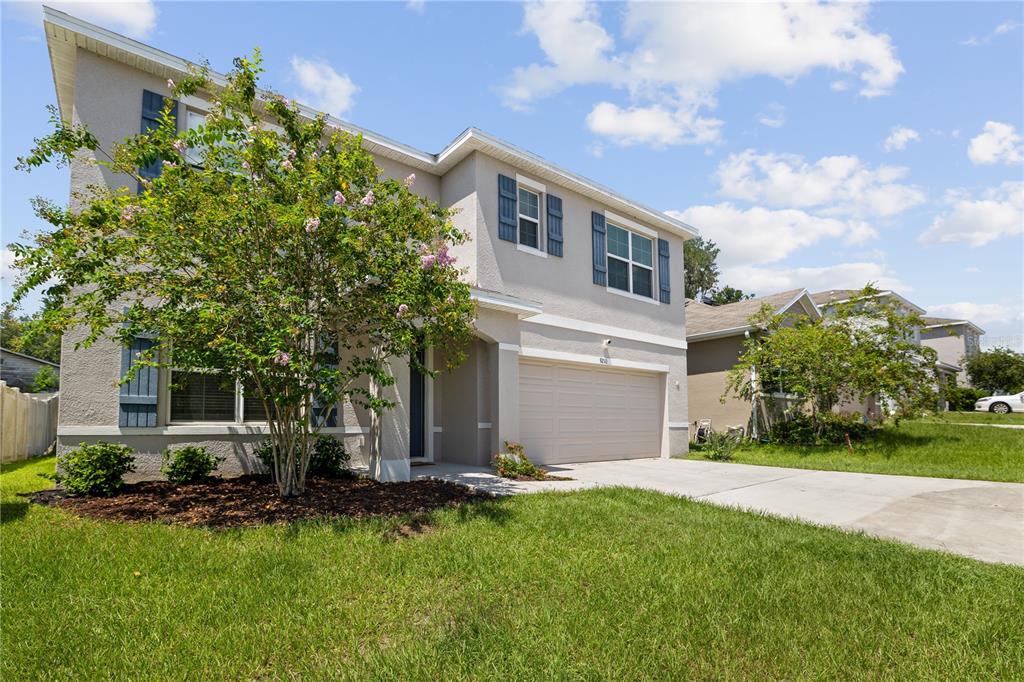 A two-story suburban house with a beige stucco exterior, blue shutters, and a concrete driveway — 9210 WATOLLA DRIVE, THONOTOSASSA, FL