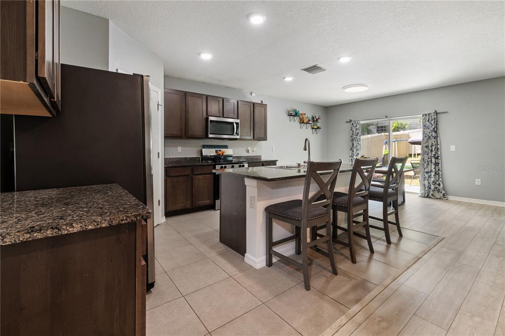 A kitchen features dark wood cabinets, granite countertops, a center island, and three bar stools — 9210 WATOLLA DRIVE, THONOTOSASSA, FL