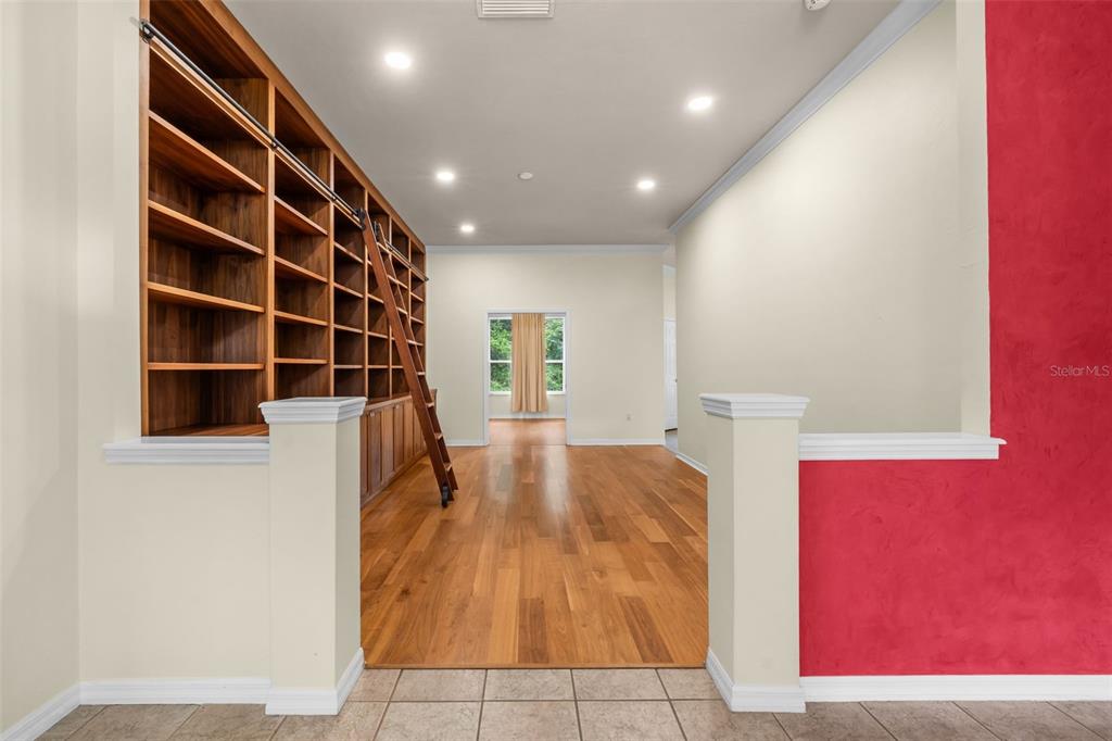 A room with hardwood floors, a large built-in wooden bookshelf, and a rolling library ladder — 2501 NW 91ST DRIVE, GAINESVILLE, FL