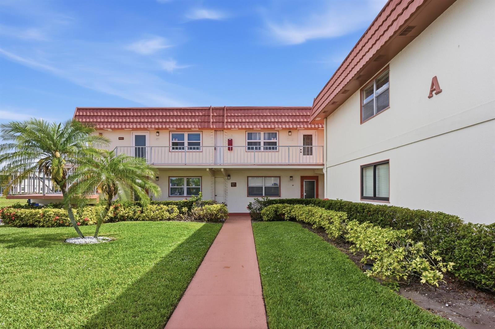 An exterior view of a two-story apartment building with a walkway and landscaped lawn — 47 Saxony A, Delray Beach FL 33446, DELRAY BEACH, FL