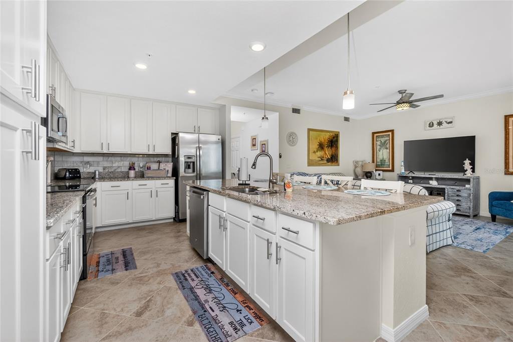 A kitchen with white cabinets, granite countertops, and a large island opens to a living area — 14081 HERITAGE LANDING BOULEVARD UNIT 232, PUNTA GORDA, FL