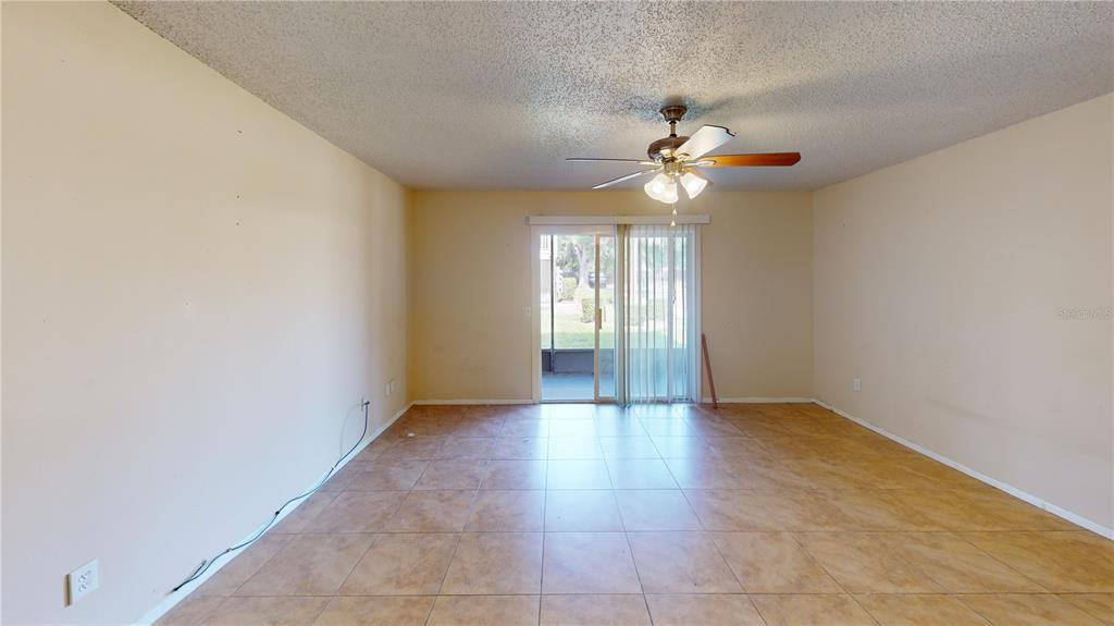 An empty room with tan tile flooring, a ceiling fan, and sliding glass doors — 4030 CORTEZ DRIVE UNIT B, TAMPA, FL