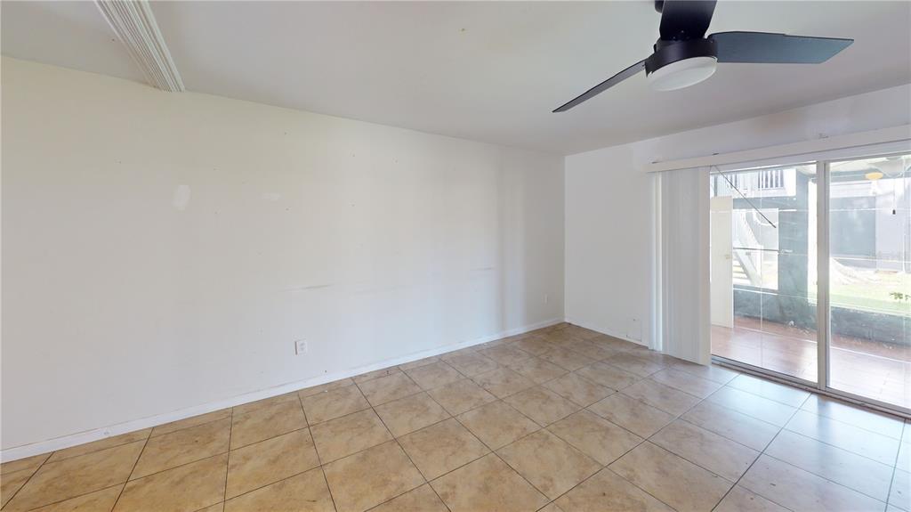 An empty room features beige tile flooring, a ceiling fan, and sliding glass patio doors — 4030 CORTEZ DRIVE UNIT B, TAMPA, FL