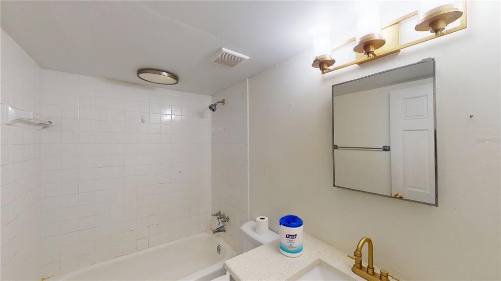 A bathroom features a white tiled shower-tub combo, a vanity with a mirror, and gold-toned fixtures — 4030 CORTEZ DRIVE UNIT B, TAMPA, FL