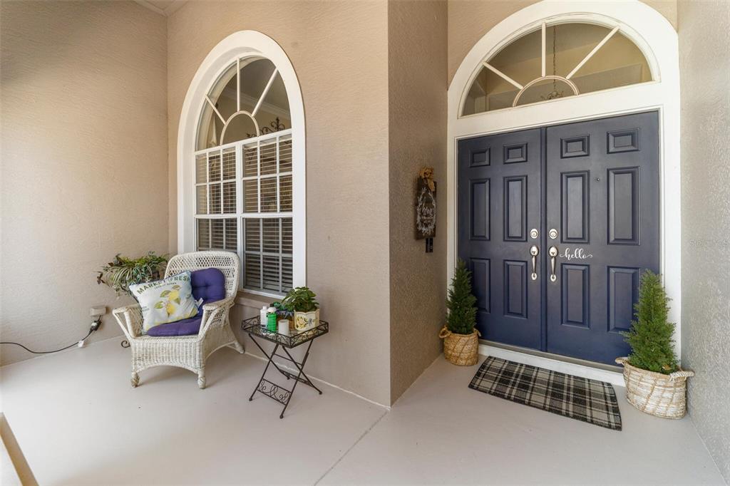 A covered front porch features a white wicker chair, a small table, and blue double doors — 1819 LATELIA COURT, TRINITY, FL
