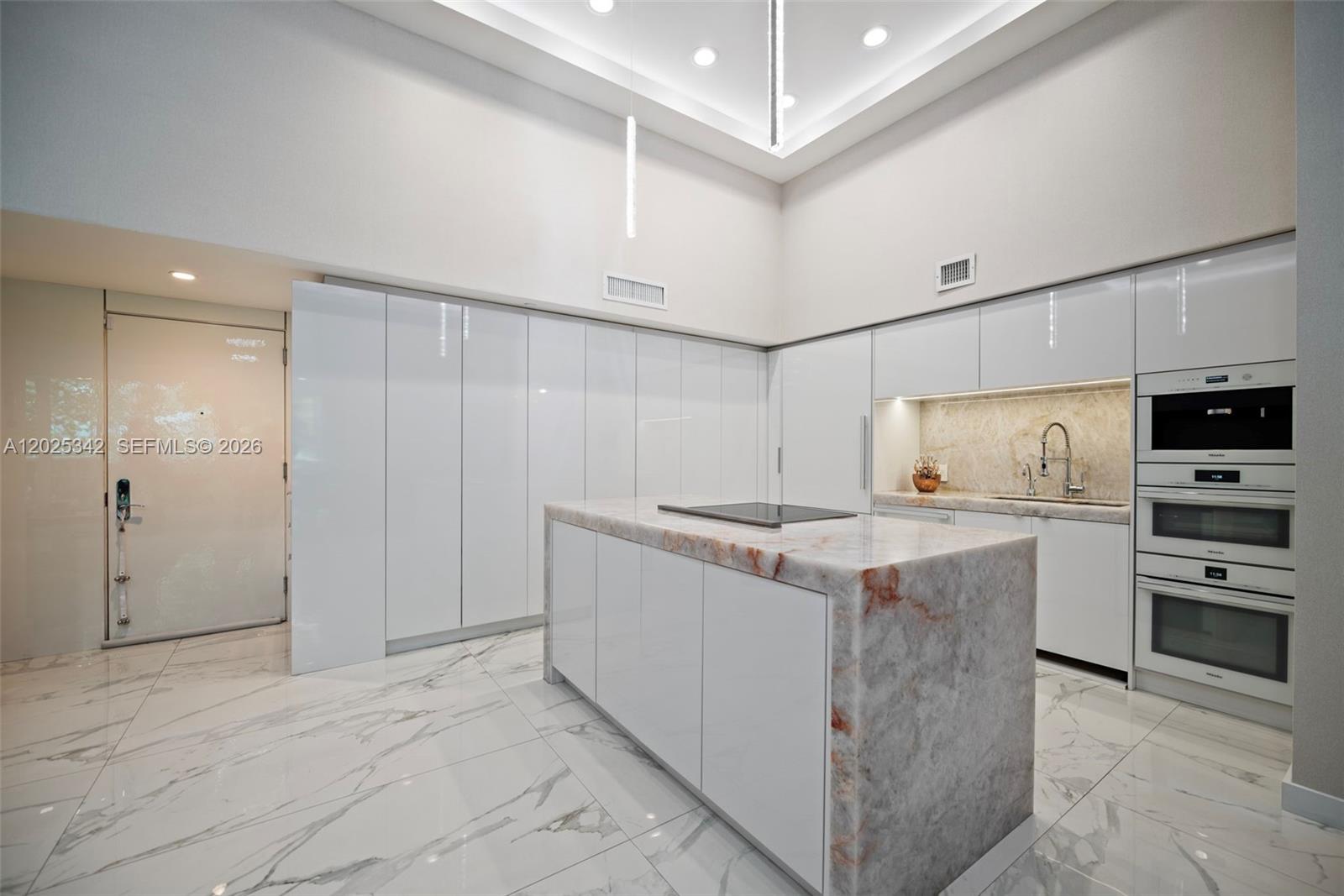 A modern kitchen features white cabinetry, a marble-topped island, and white marble-patterned tile flooring — 1800 S Ocean Dr # 310, Hallandale Beach FL 33009, HALLANDALE BEACH, FL