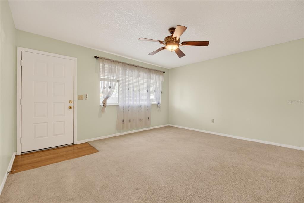 A living room with beige carpet, light green walls, a ceiling fan, and a front door — 8720 SW 108TH LANE, OCALA, FL