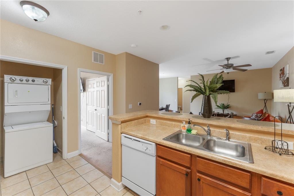 A kitchen with a double sink and dishwasher overlooks a living area with a ceiling fan — 3174 FELTRIM PLACE UNIT 201, KISSIMMEE, FL