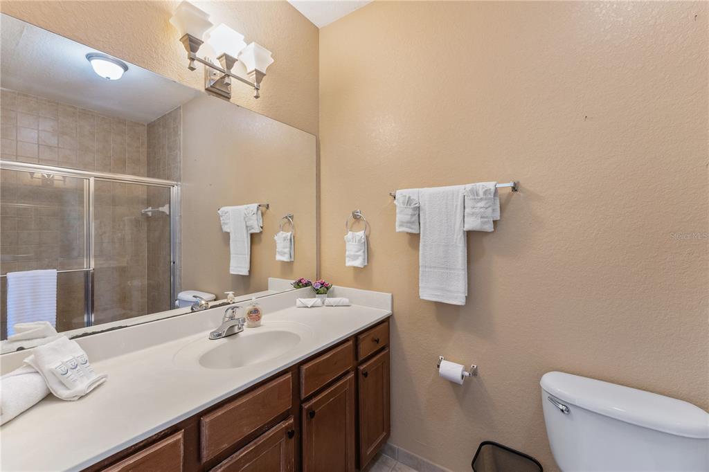 A bathroom features a single-sink vanity with dark wood cabinets and a large wall mirror — 3174 FELTRIM PLACE UNIT 201, KISSIMMEE, FL