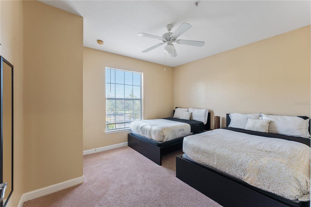 A bedroom features two beds with black frames, beige walls, and a ceiling fan — 3174 FELTRIM PLACE UNIT 201, KISSIMMEE, FL