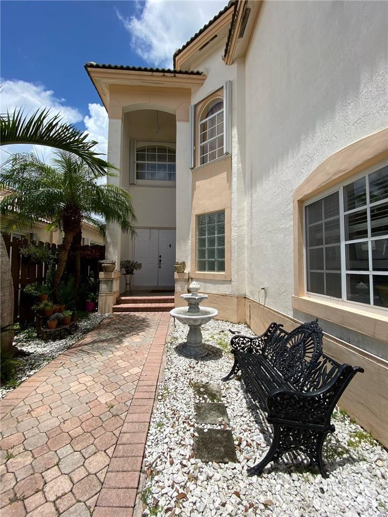 An exterior view shows a house entrance with a stone walkway, fountain, and black bench — 10747 NW 70th Terrace, Doral FL 33178, DORAL, FL