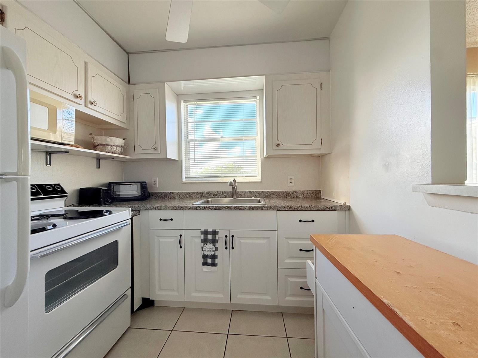 A kitchen features white cabinets, a granite countertop, a stainless steel sink, and white appliances — 204 Oakridge M # 204, Deerfield Beach FL 33442, DEERFIELD BEACH, FL