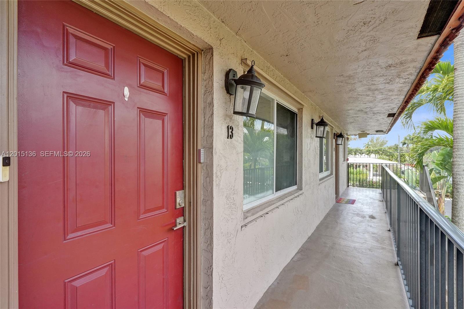 A red front door with the number 13 sits on an outdoor apartment walkway — 3050 NE 5th Ter # 13, Wilton Manors FL 33334, WILTON MANORS, FL