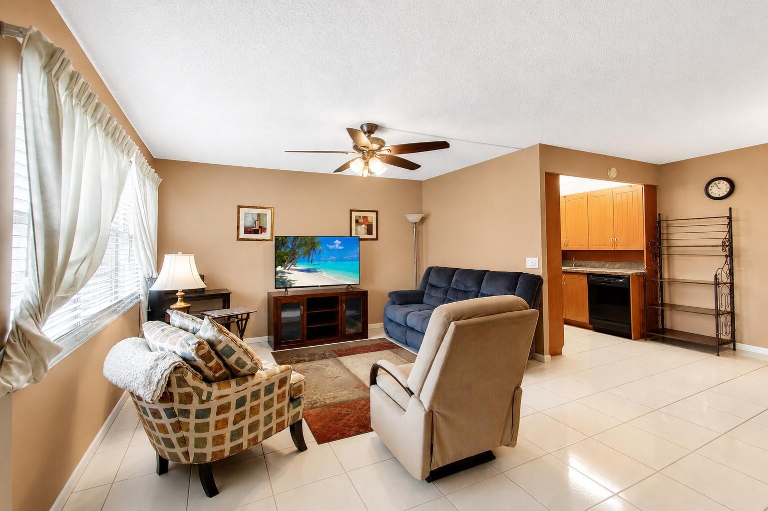A living room with a blue sofa, patterned armchair, beige recliner, and an open kitchen — 3008 Cornwall A, Boca Raton FL 33434, BOCA RATON, FL