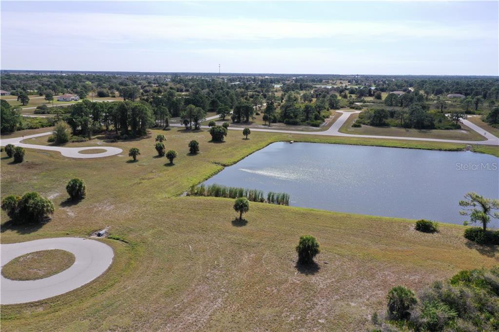 An aerial view shows a grassy lot next to a pond and paved roads — 1 TARPON COURT, PLACIDA, FL