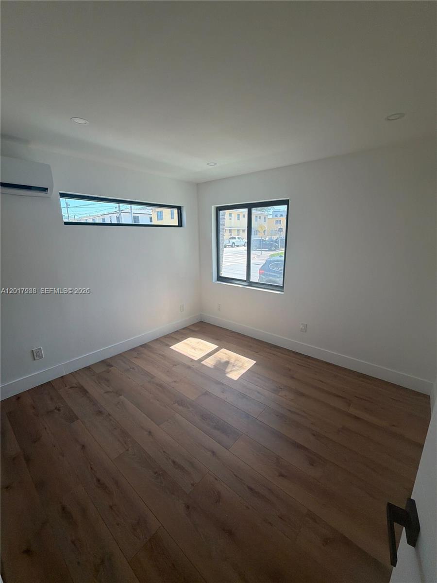 An empty room features wood-look flooring, white walls, a mini-split unit, and two windows — 7801 Byron Ave # B, Miami Beach FL 33141, MIAMI BEACH, FL