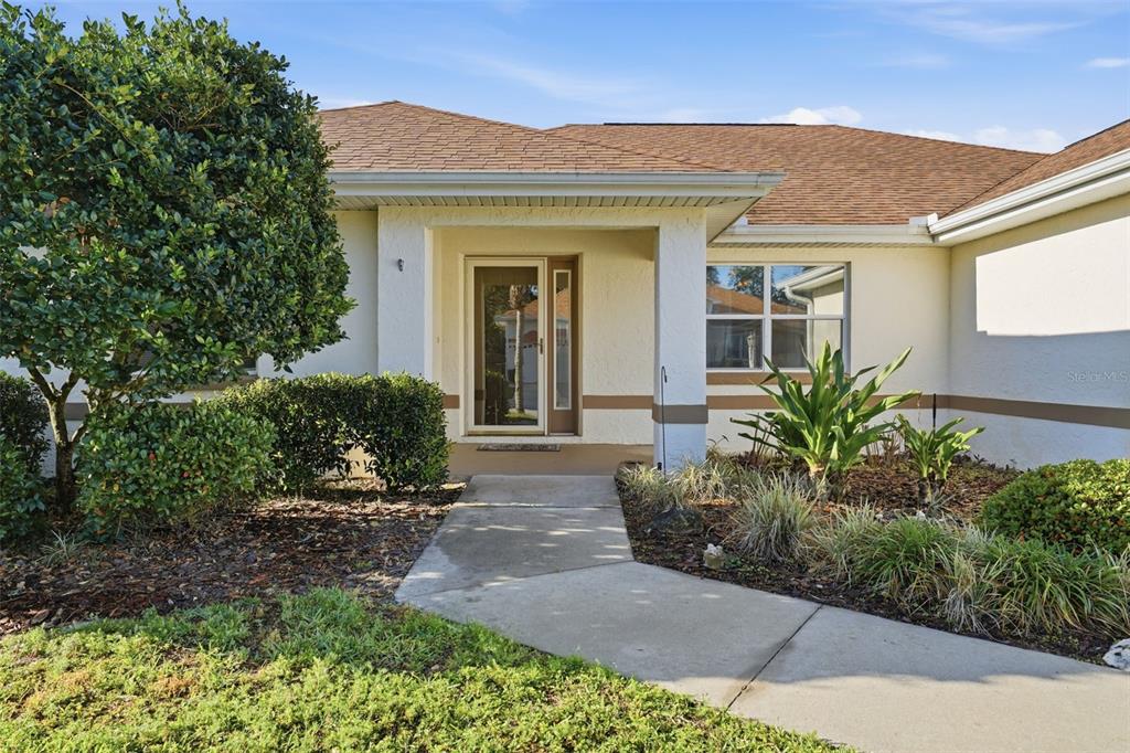 A concrete walkway leads to the front entrance of a single-story house with landscaping — 17083 SE 115TH TERRACE ROAD, SUMMERFIELD, FL