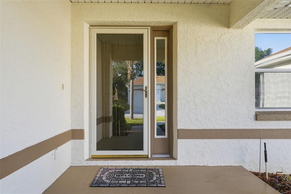 A front entryway features a glass storm door, a side light, and a welcome mat — 17083 SE 115TH TERRACE ROAD, SUMMERFIELD, FL