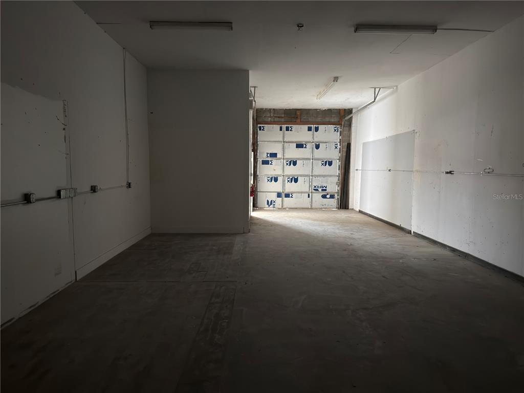 An empty commercial space features concrete floors, white walls, and a large metal roll-up door — 18210 PAULSON DRIVE UNIT 7, PORT CHARLOTTE, FL