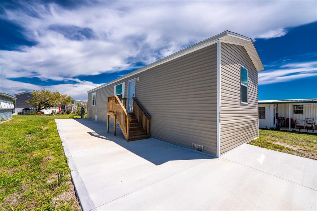 A tan mobile home with a concrete driveway and wooden stairs leading to the entrance — 7400 BECKLEY STREET, PORT CHARLOTTE, FL