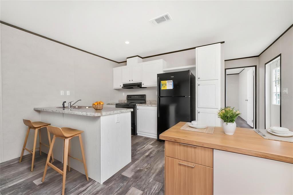 A kitchen features white cabinets, a black refrigerator, a breakfast bar, and wood-look flooring — 7400 BECKLEY STREET, PORT CHARLOTTE, FL