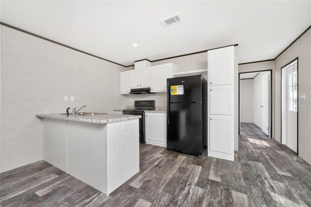 A kitchen features white cabinets, a black refrigerator, a kitchen island, and wood-look flooring — 7400 BECKLEY STREET, PORT CHARLOTTE, FL