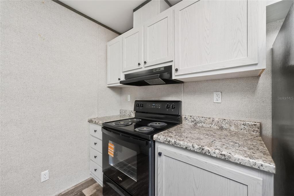 A kitchen features white cabinets, a black stove, and speckled laminate countertops — 7400 BECKLEY STREET, PORT CHARLOTTE, FL