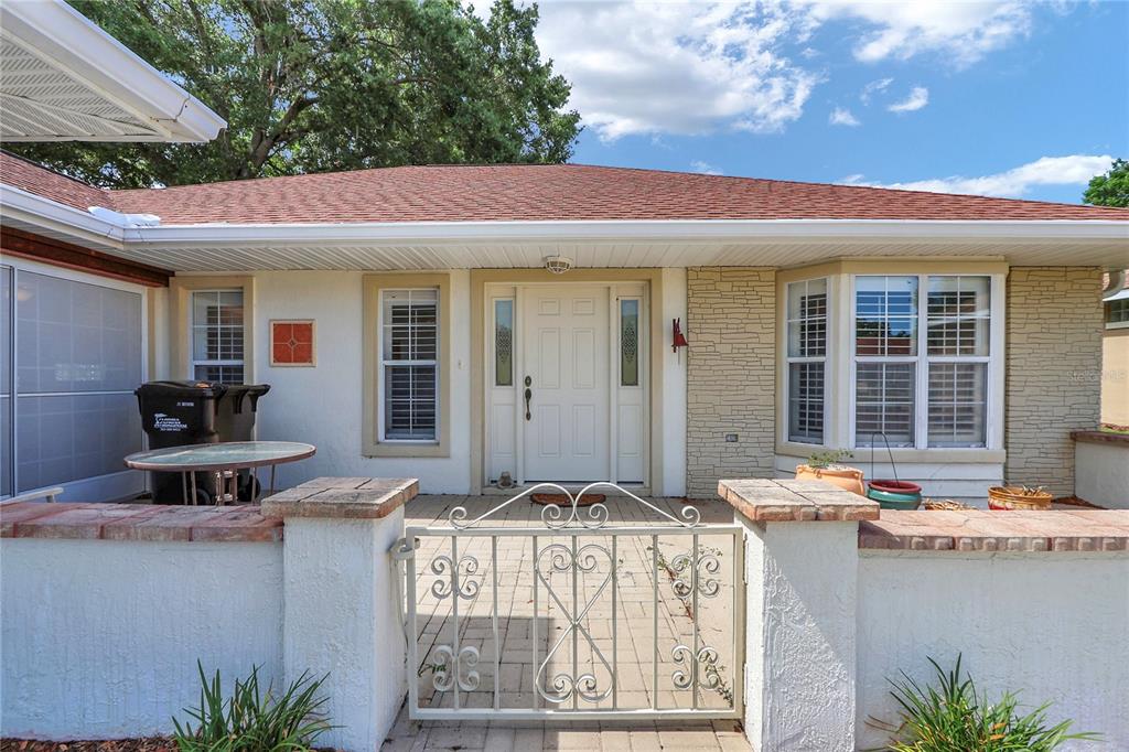 The exterior of a single-story house features a gated courtyard, white stucco walls, and stone accents — 7279 SW 115 PLACE, OCALA, FL