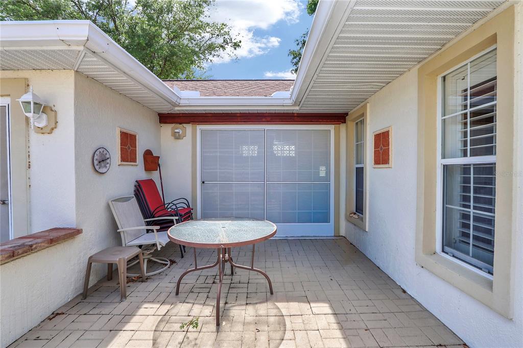 A paved outdoor patio features a glass-topped table, chairs, and a sliding screen door — 7279 SW 115 PLACE, OCALA, FL