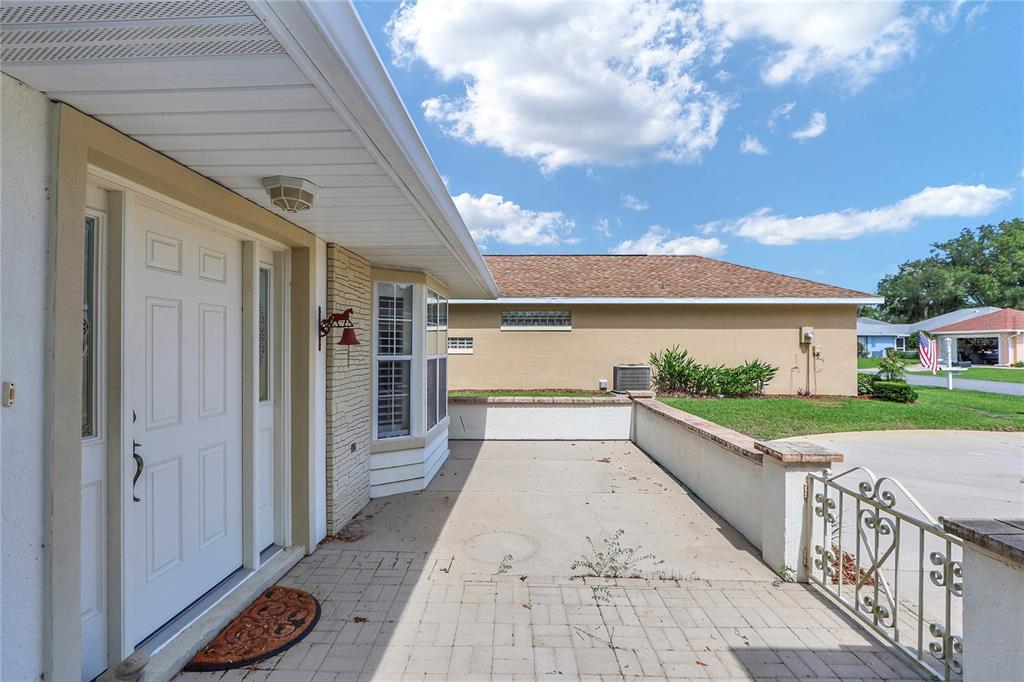 A paved front porch features a white door, a brick accent wall, and a metal railing — 7279 SW 115 PLACE, OCALA, FL