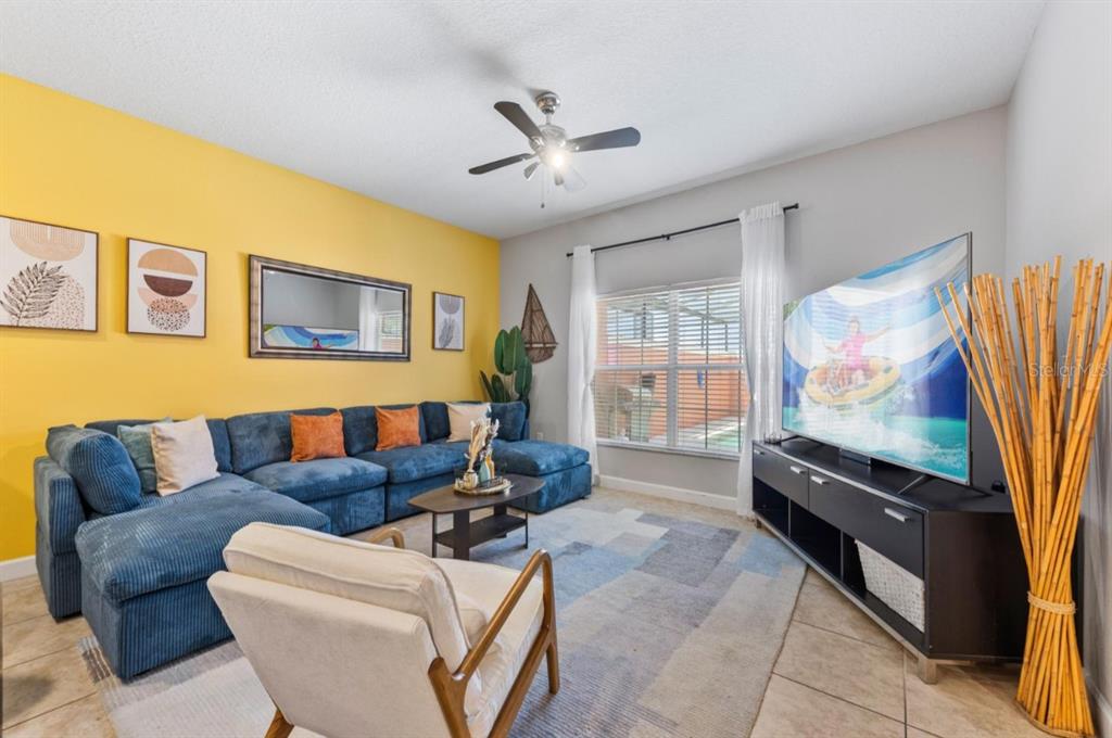 A living room features a blue sectional sofa, a yellow accent wall, and a television — 8847 CANDY PALM ROAD, KISSIMMEE, FL