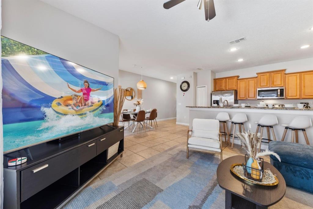 A living room with a large television, tile flooring, and an open kitchen with bar seating — 8847 CANDY PALM ROAD, KISSIMMEE, FL