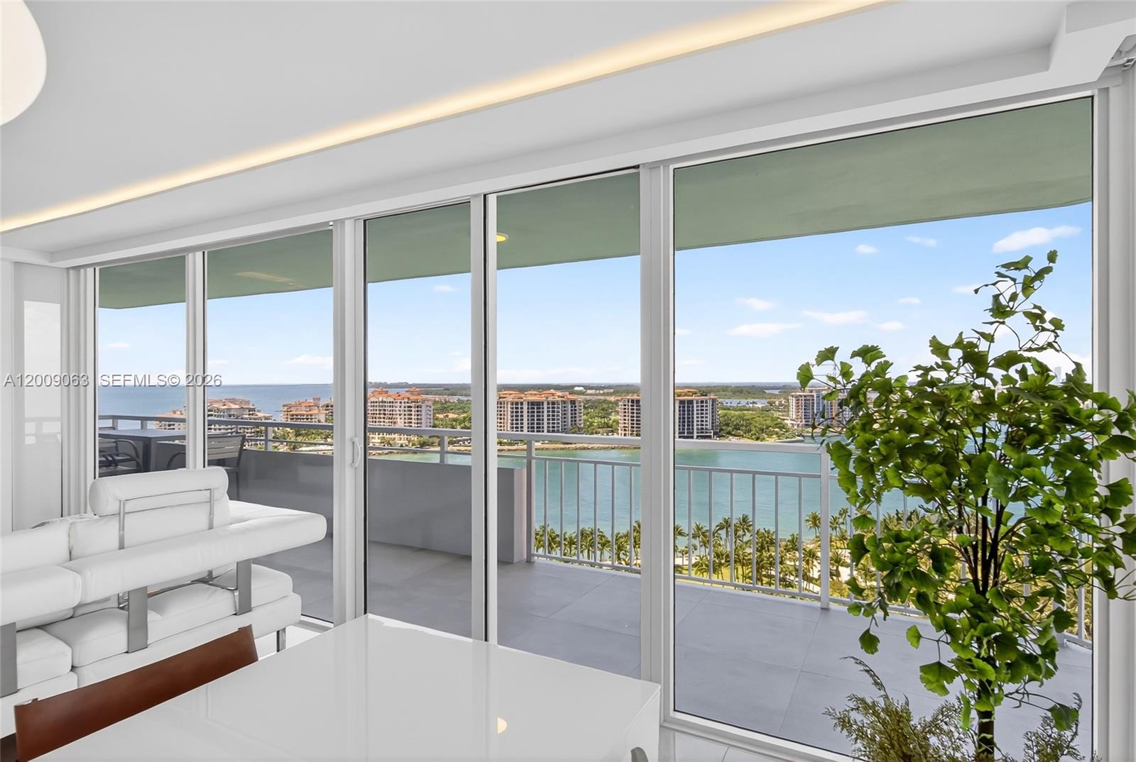 A bright room features floor-to-ceiling sliding glass doors overlooking a balcony, water, and buildings — 400 S Pointe Dr # 2009, Miami Beach FL 33139, MIAMI BEACH, FL