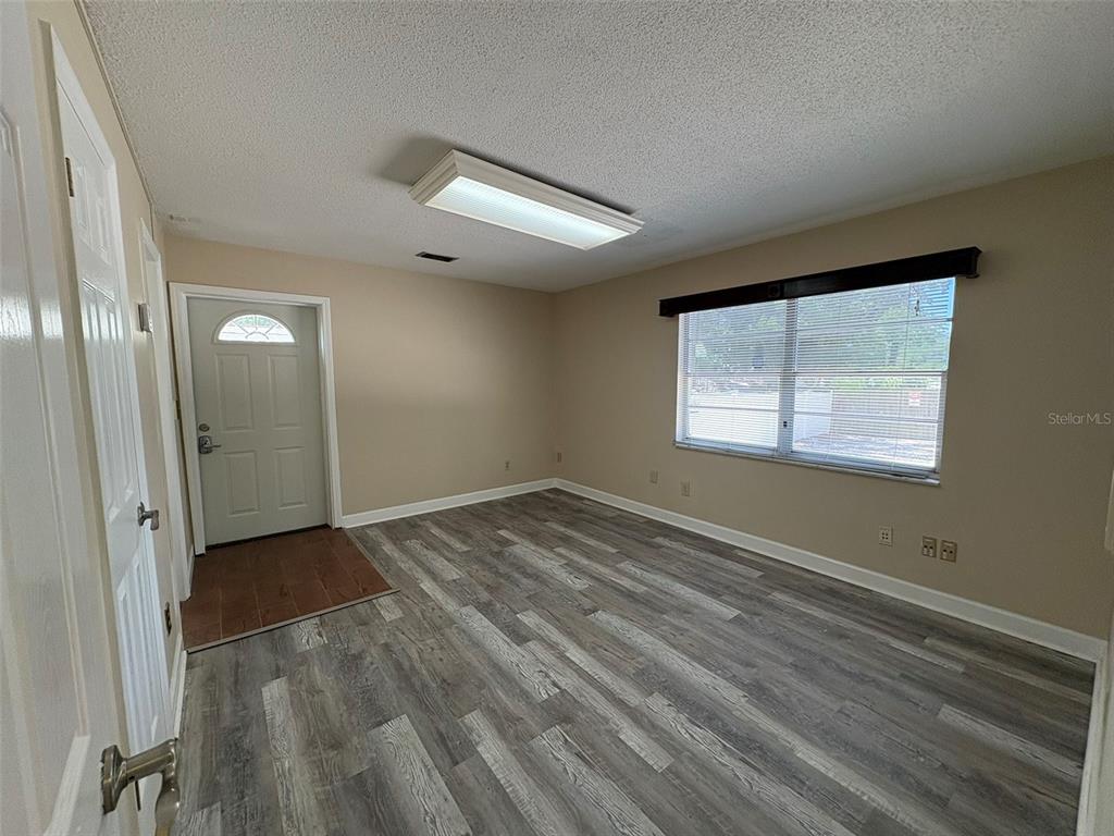 An empty room features gray wood-look flooring, beige walls, a large window, and a ceiling light — 264 E ALTAMONTE DRIVE, ALTAMONTE SPRINGS, FL