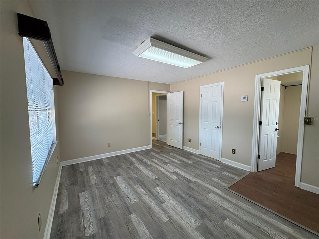A bedroom with gray wood-look flooring, beige walls, a ceiling light fixture, and three doors — 264 E ALTAMONTE DRIVE, ALTAMONTE SPRINGS, FL