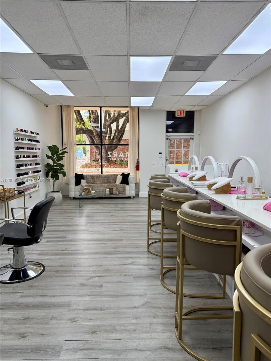 A bright nail salon features a seating area, manicure stations with stools, and wood-look flooring — CORAL GABLES, FL