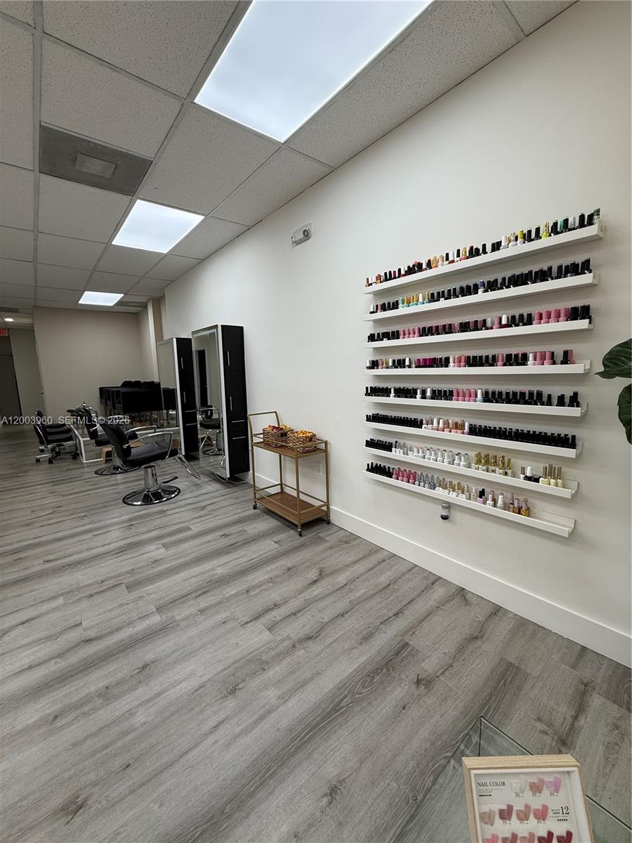 A salon interior features light wood-look flooring, white walls, styling chairs, and wall-mounted nail polish shelves — CORAL GABLES, FL