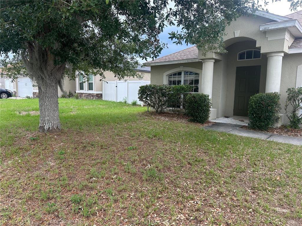 A front view of a house with a large tree, lawn, and covered entryway — 451 PEACE COURT, KISSIMMEE, FL