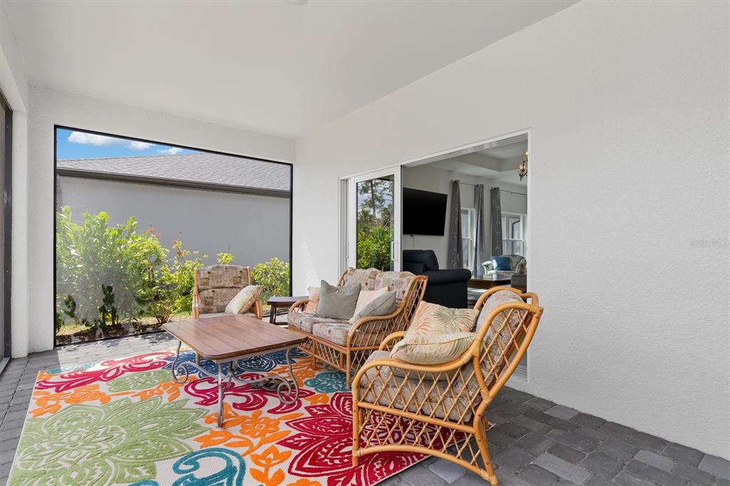 A covered patio features wicker furniture, a colorful patterned rug, and a screened-in view — 1736 SUNSET PRESERVE WAY, PORT CHARLOTTE, FL