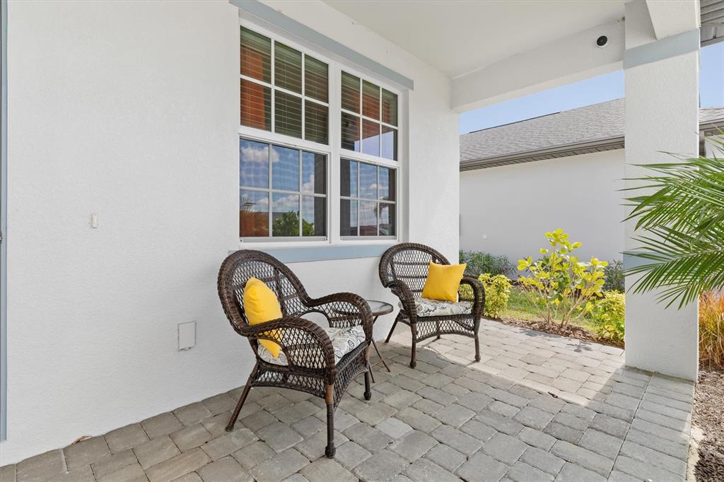 A patio features two wicker chairs with yellow pillows on a paved stone floor — 1736 SUNSET PRESERVE WAY, PORT CHARLOTTE, FL