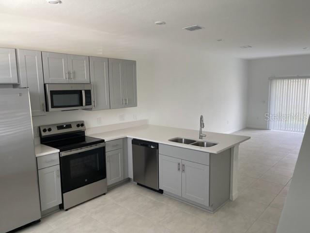 A modern kitchen features gray cabinets, stainless steel appliances, and white countertops — 3158 SKYLINE LOOP, KISSIMMEE, FL