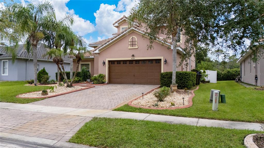 A two-story suburban house with a tan stucco exterior, a brown garage door, and landscaping — 4089 NAVIGATOR WAY, KISSIMMEE, FL